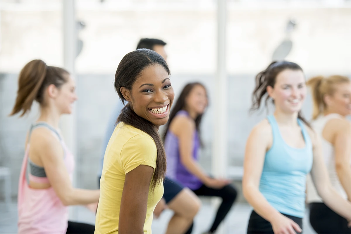 Group fitness class with smiling participants engaging in exercises to reduce anxiety and stress, promoting mental well-being through physical activity.